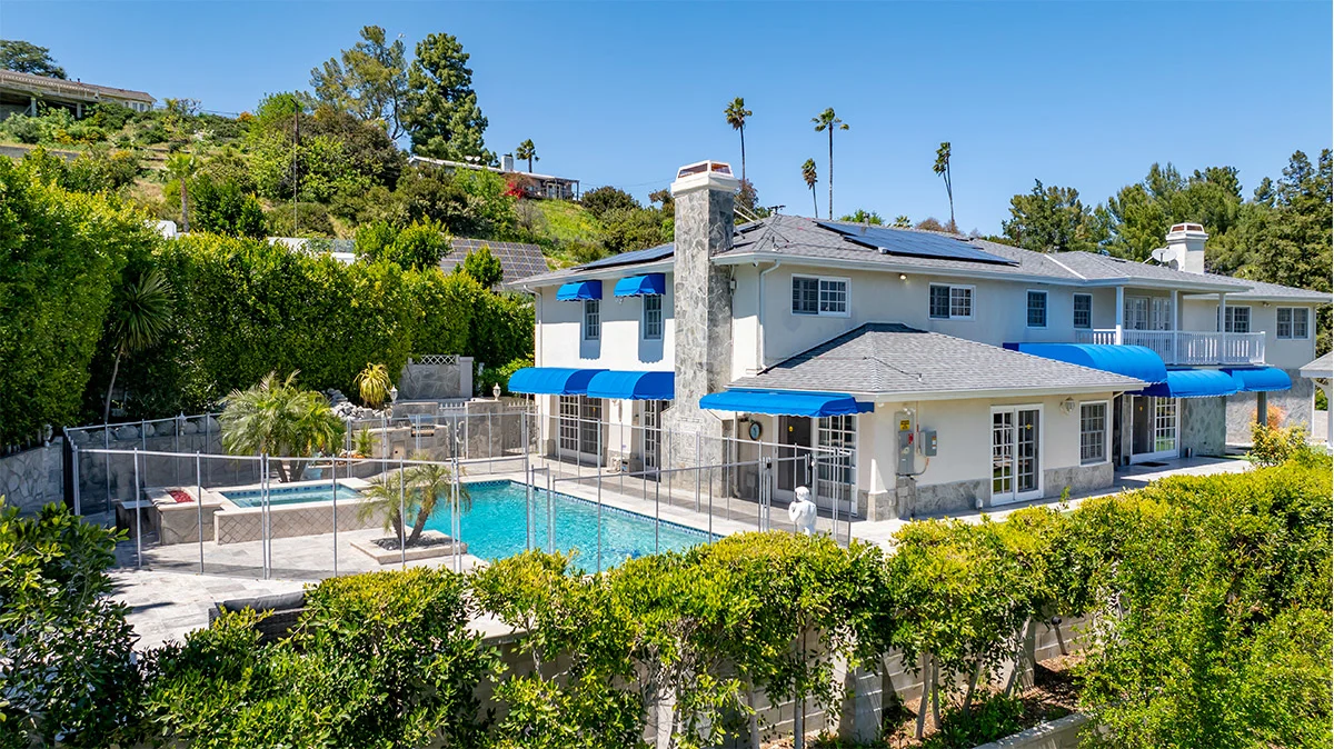 A rehab facility with a pool, blue awnings, and lush greenery.