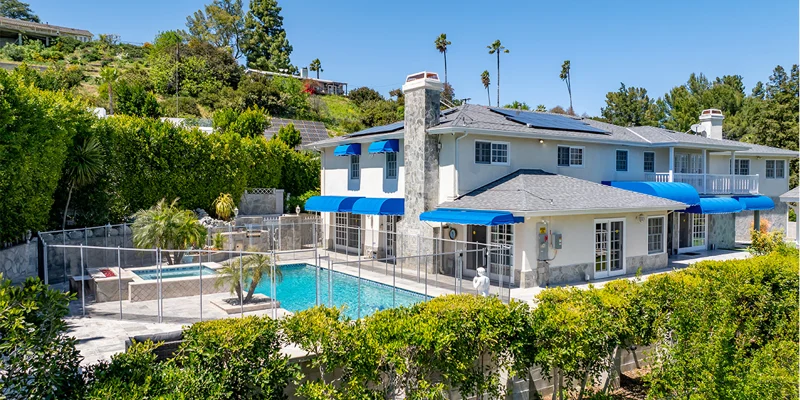 A rehab facility with a pool, blue awnings, and lush greenery.