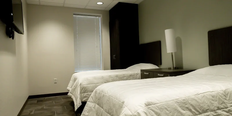 A modern rehab bedroom with two twin beds, a TV, and soft lighting.