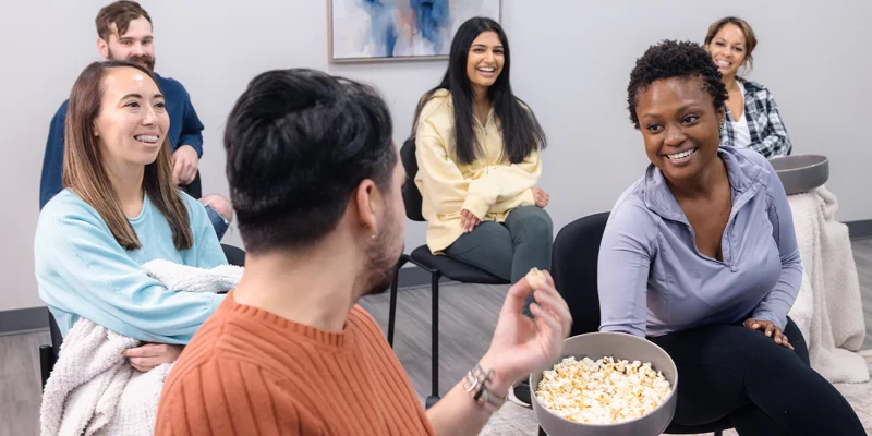 A group of people laughing while sharing snacks in a therapy session.