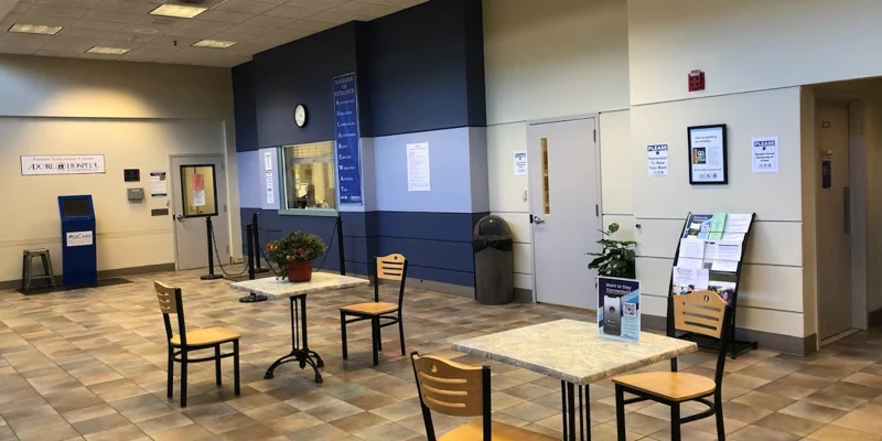 Lobby with wooden chairs around tables, and potted plants.