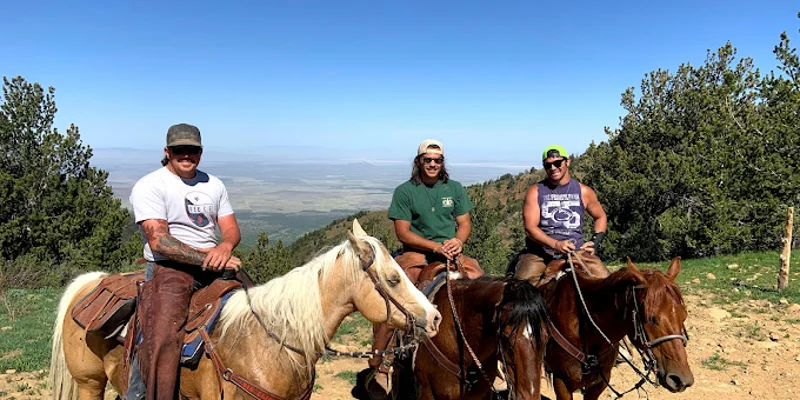 Three men on horses smiling on a green hillside with blue sky above.