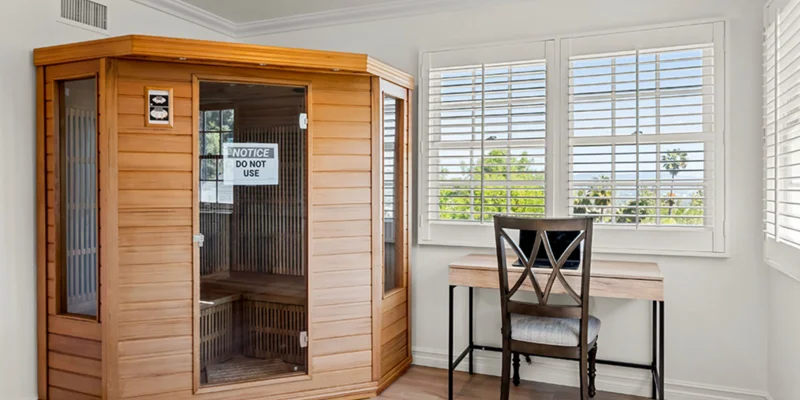 A room with a wooden sauna, desk, and large windows.