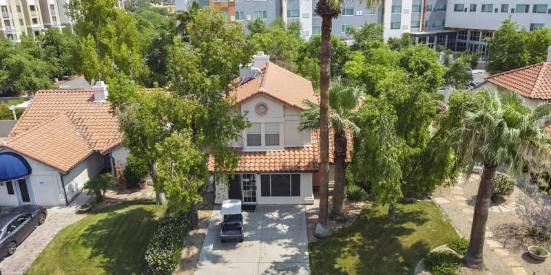 Two-story house with a red tile roof, around palm trees,