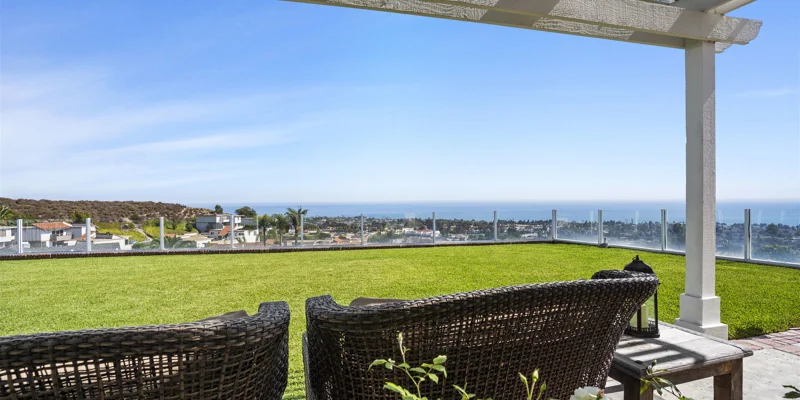 Outdoor seating area with ocean views, green grass, and glass railing.