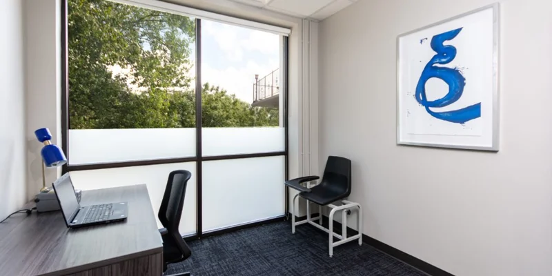 A private office with a desk, laptop, and a blue chair.