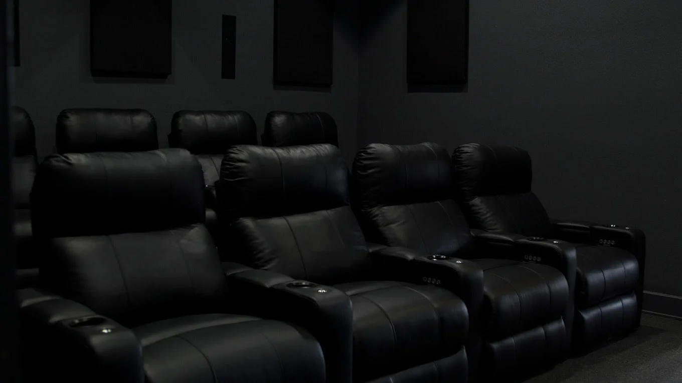 A dark home theater with black reclining chairs.