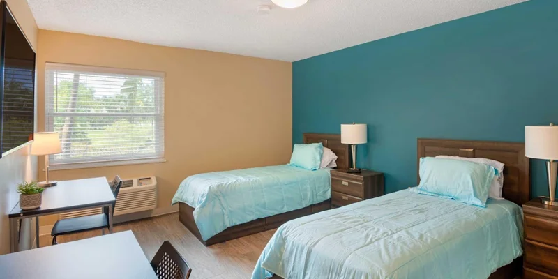 Bright bedroom with twin beds, desk, and decorative artwork.