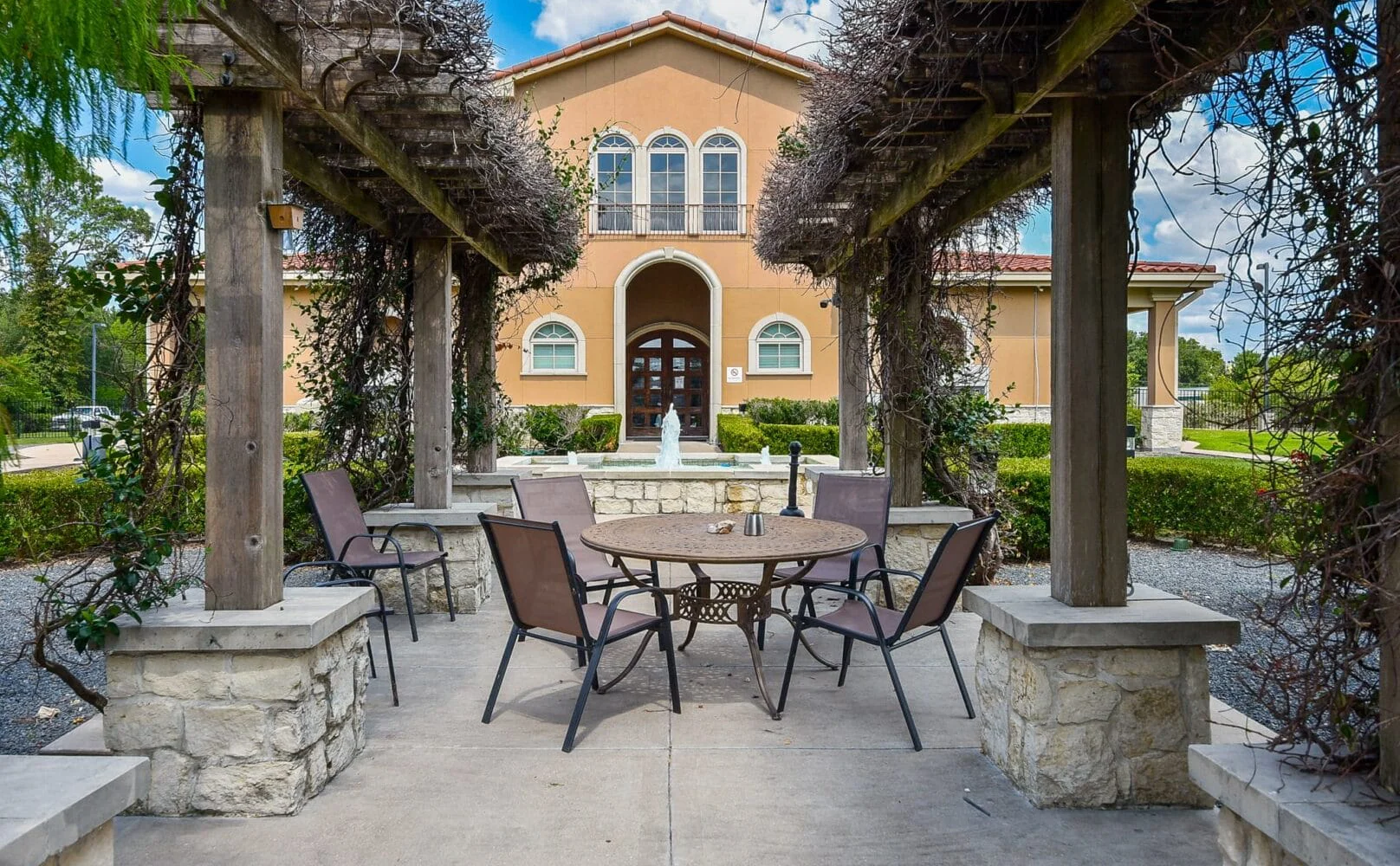 a wooden pergola, surrounded by greenery, and a fountain.