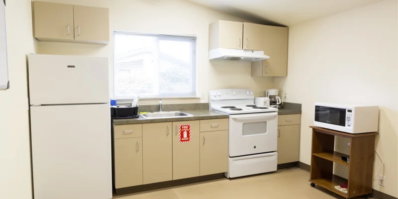 A small kitchen with beige cabinets, a stove, microwave, and fridge.