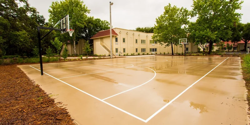 An outdoor basketball court surrounded by trees and a beige building