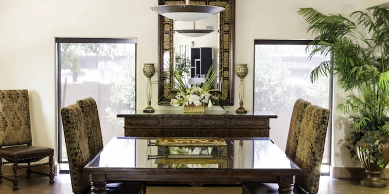 Dinning room with a plant, long table and large windows.