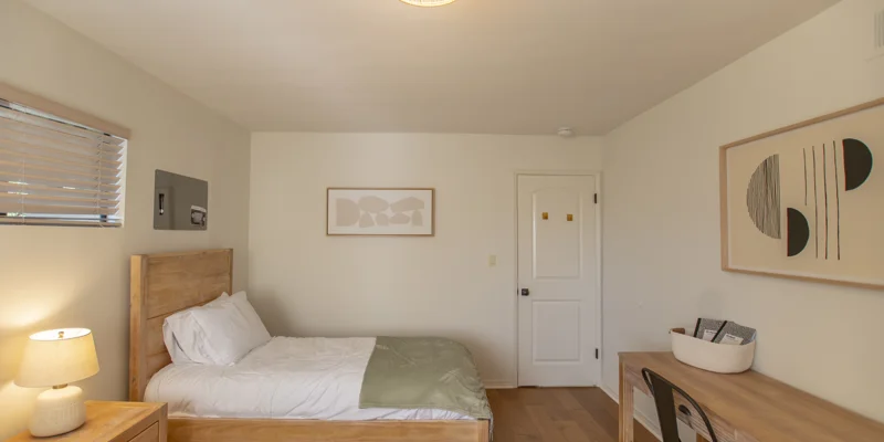 A private bedroom with a wooden bed, desk, and neutral decor.