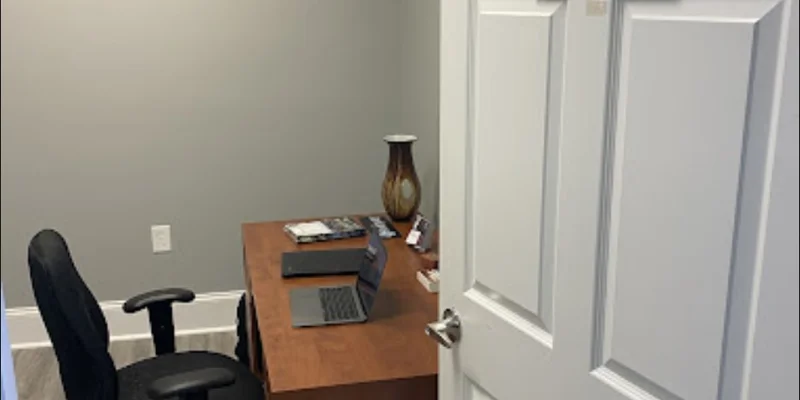 A small office with a wooden desk, black chair, and an open laptop