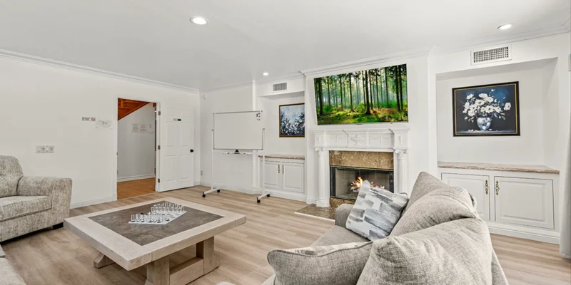 A common room with a fireplace, whiteboard, and cozy seating.