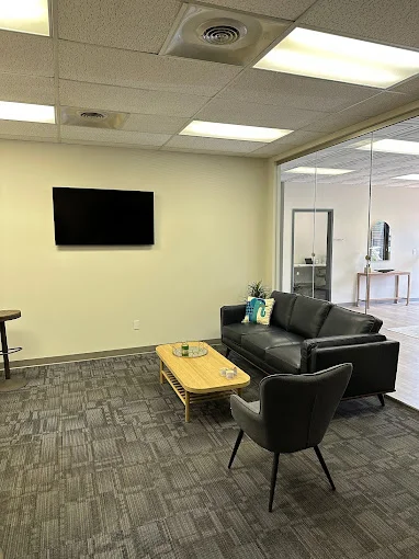 A modern waiting area with a black couch, armchair, and mounted TV.