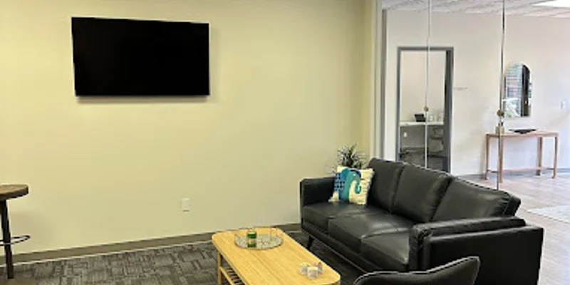 A modern waiting area with a black couch, armchair, and mounted TV.