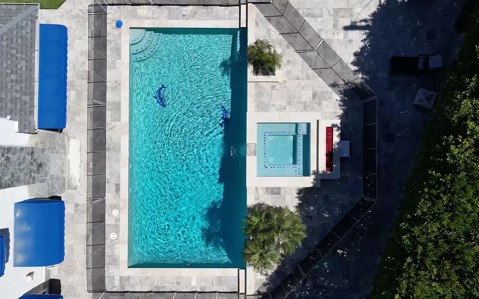 Aerial view of a fenced pool and hot tub surrounded by greenery.