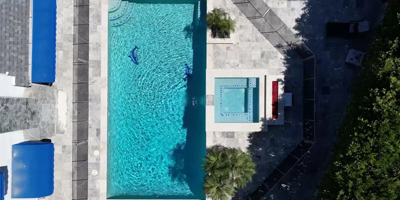 Aerial view of a fenced pool and hot tub surrounded by greenery.