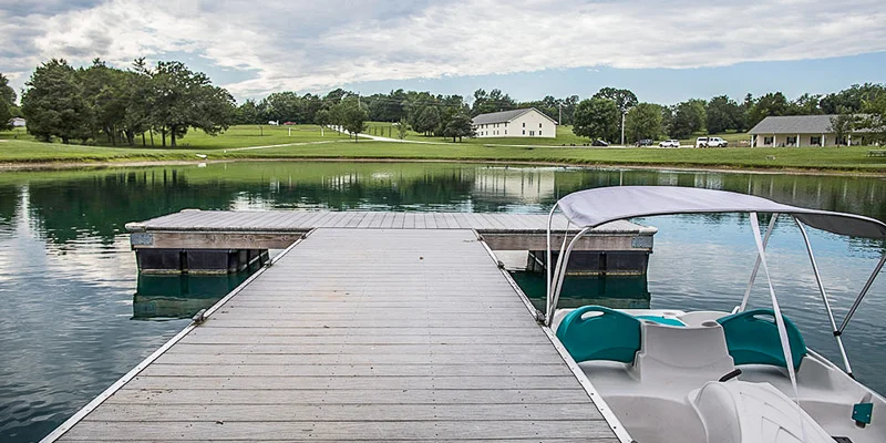A dock extending over a lake with a paddle boat tied to it.