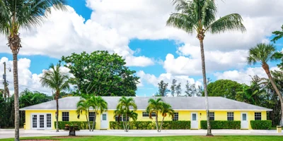 Yellow rehab facility with palm trees and lawn.