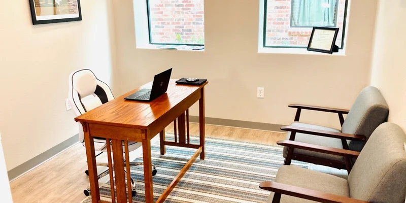 A private counseling office with a wooden desk, chairs, and natural lighting.