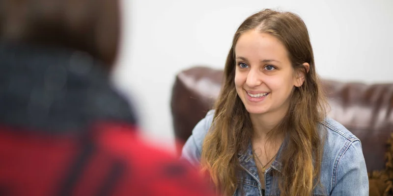 A smiling woman in a denim jacket during a one-on-one conversation.