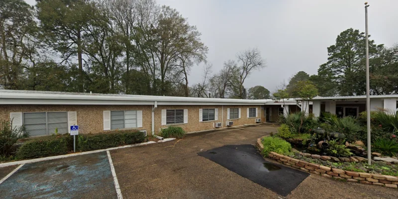 A welcoming brick building with large windows and a well-maintained lawn, with trees and shrubs.