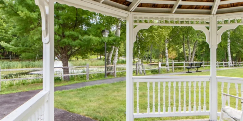 Gazebo overlooking a path, greenery, and a wooden fence.