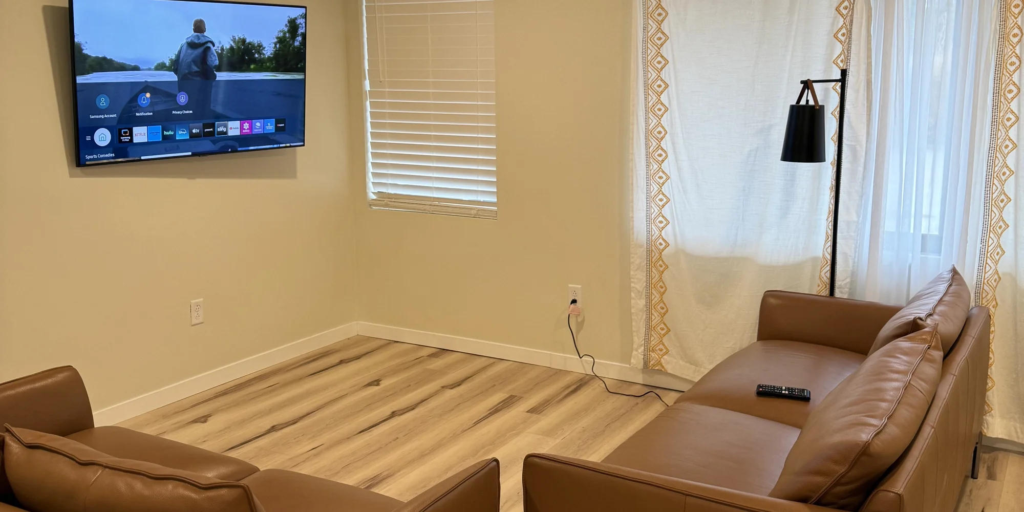 Living room with wall-mounted TV, leather sofa, and floor lamp.