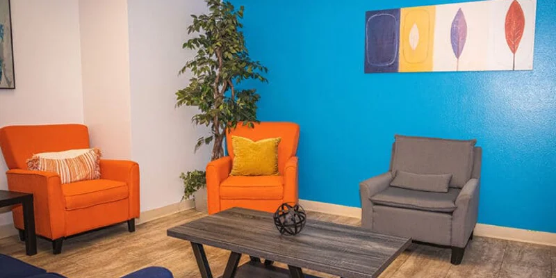A lounge area with orange chairs, a gray armchair, and a blue accent wall.
