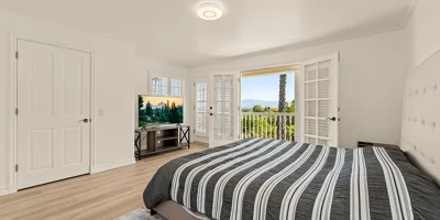 A bright bedroom with a balcony and scenic hillside views.