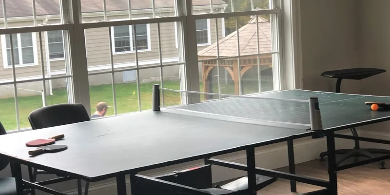 A recreation room with a ping pong table and large windows.