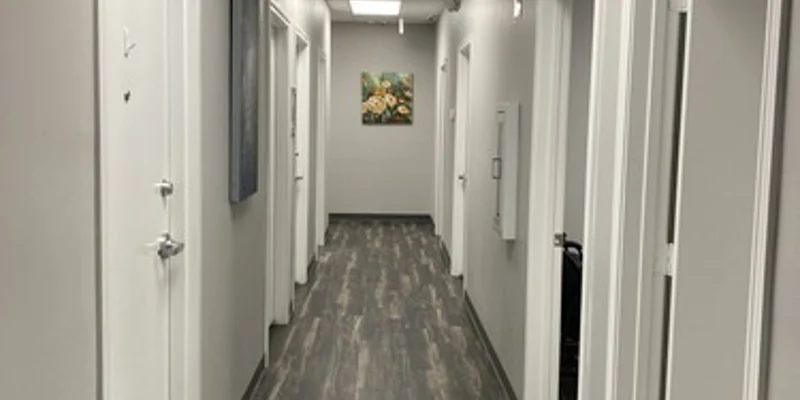 A hallway with white doors and gray flooring in a medical facility.