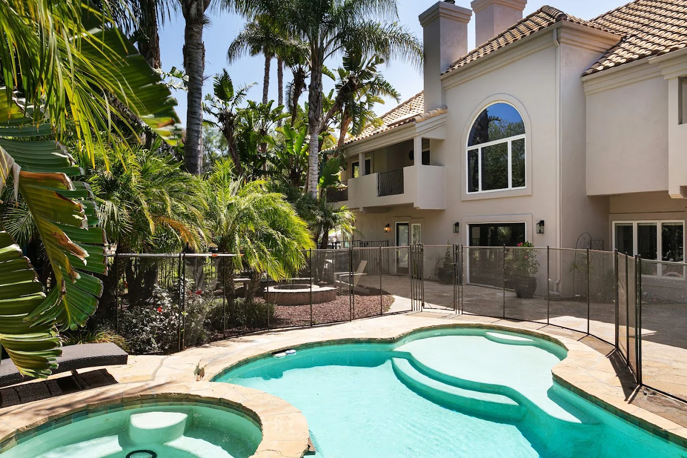 Outdoor pool area with palm trees and a fenced patio beside a villa.