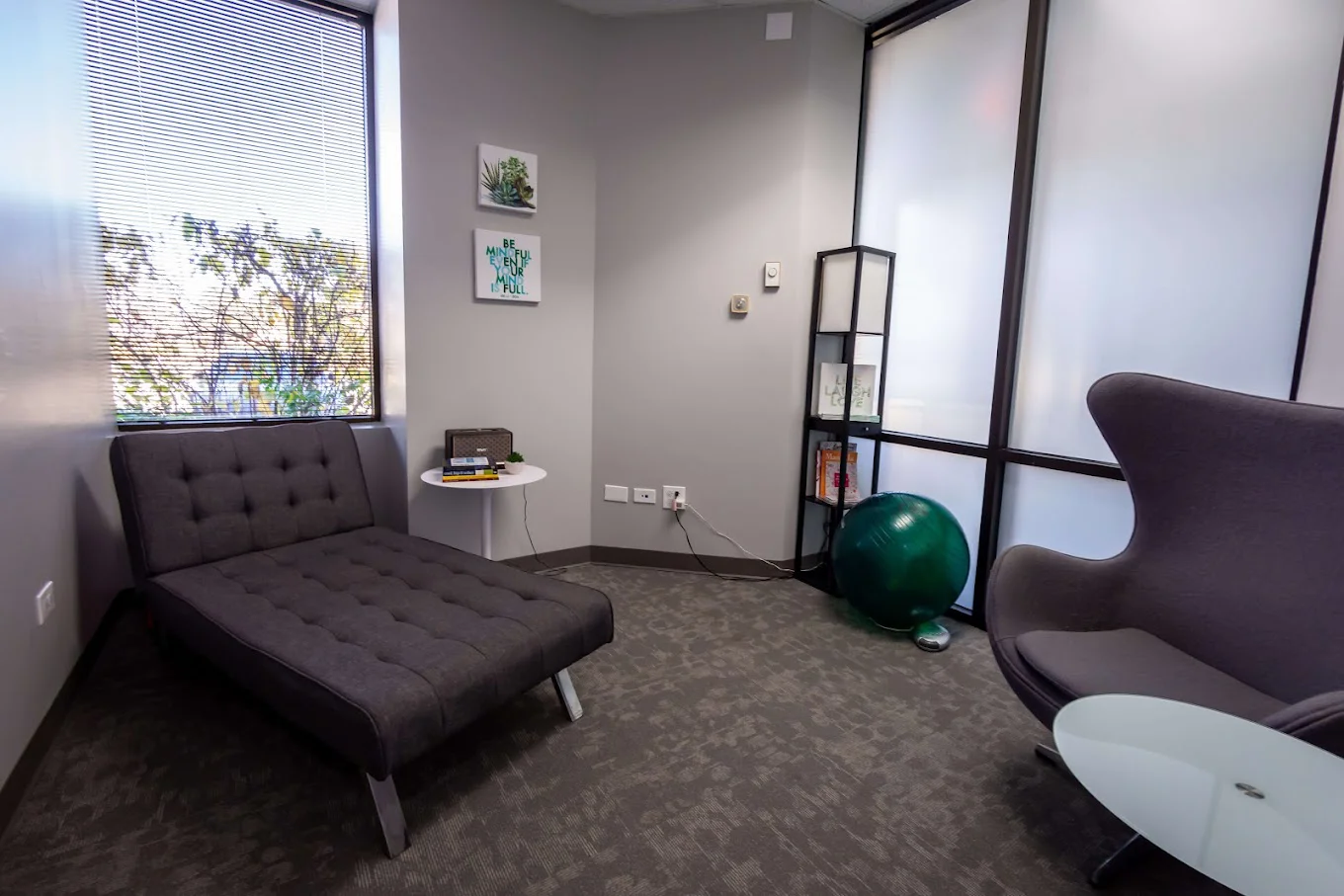 Therapy room with a gray chaise, modern chair,  and large windows.