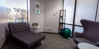 Therapy room with a gray chaise, modern chair,  and large windows.