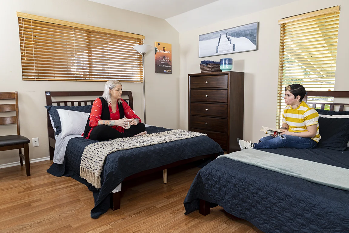 Rehab bedroom with two beds, wooden furniture, and natural light.