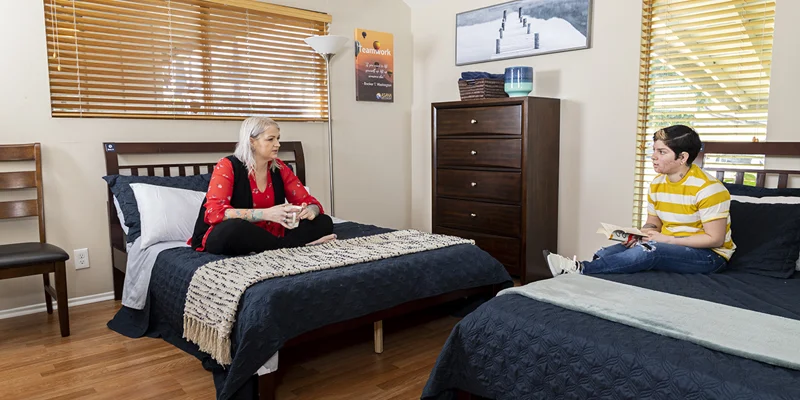 Rehab bedroom with two beds, wooden furniture, and natural light.