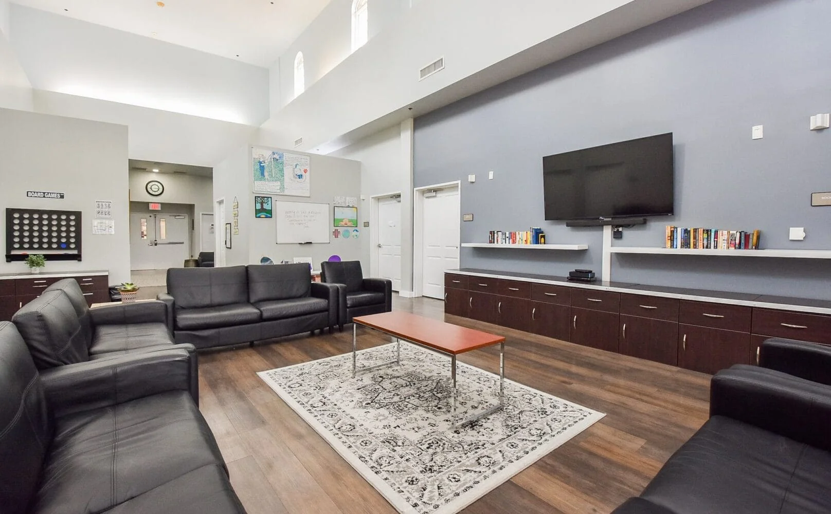 Common room with leather seating, a large TV, and bookshelves.