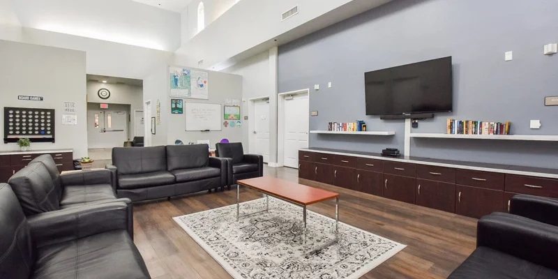 Common room with leather seating, a large TV, and bookshelves.