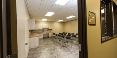 Group therapy room with rows of black chairs and kitchenette in the background
