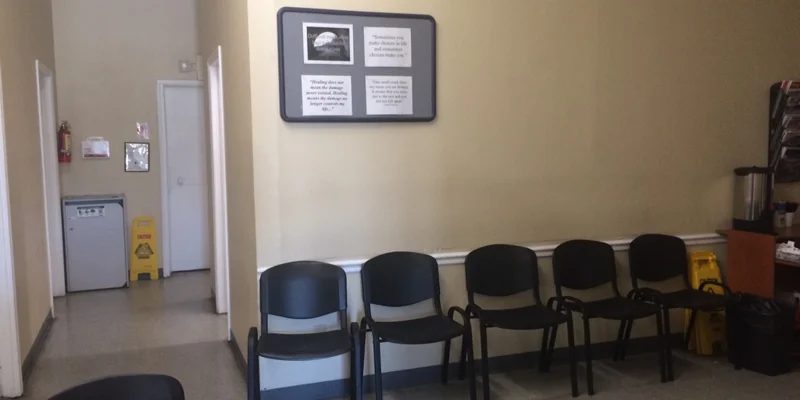 A waiting area with black chairs, a bulletin board, and a coffee station.