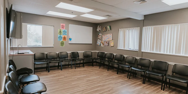 Group therapy room with black chairs in a circle, a TV and a board.