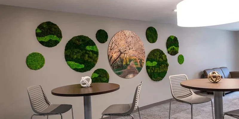 A dining area with round tables and a wall decorated with green art.