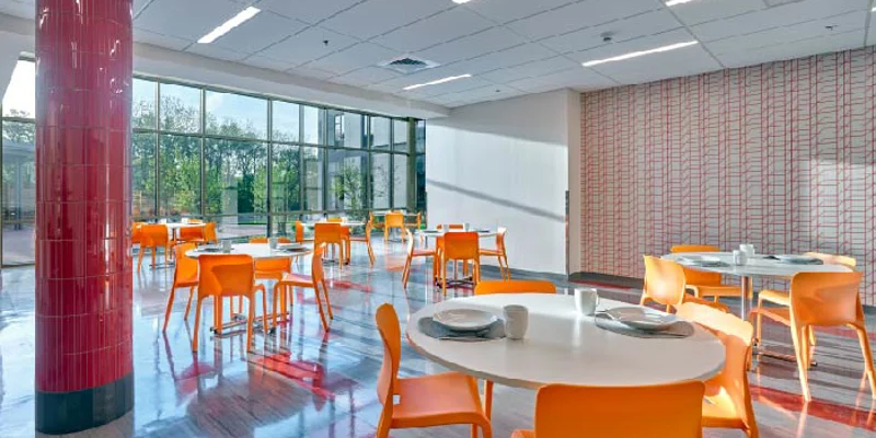 Dining lounge with tables and chairs near large windows.