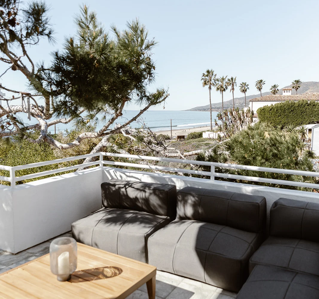 Rooftop seating area with ocean and palm tree views.