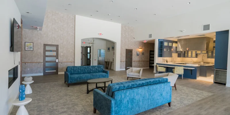 Lounge with blue couches, a modern kitchen, and bright lighting.