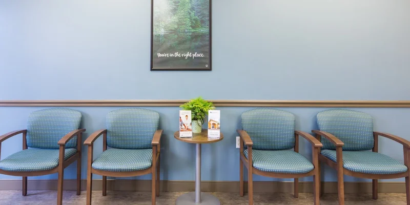 Waiting area with blue chairs, a round table, and a framed wall poster.