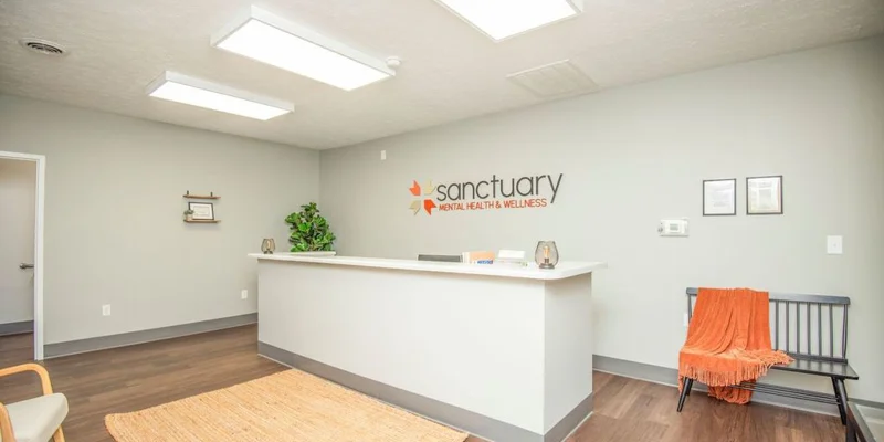 Reception area with white desk, bench, and Sanctuary logo on wall